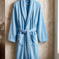 TORK cotton Turkish bathrobe hanging on a wooden hook, soft and plush fabric, beige color, cozy and comfortable for lounging.