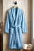 TORK cotton Turkish bathrobe hanging on a wooden hook, soft and plush fabric, beige color, cozy and comfortable for lounging.